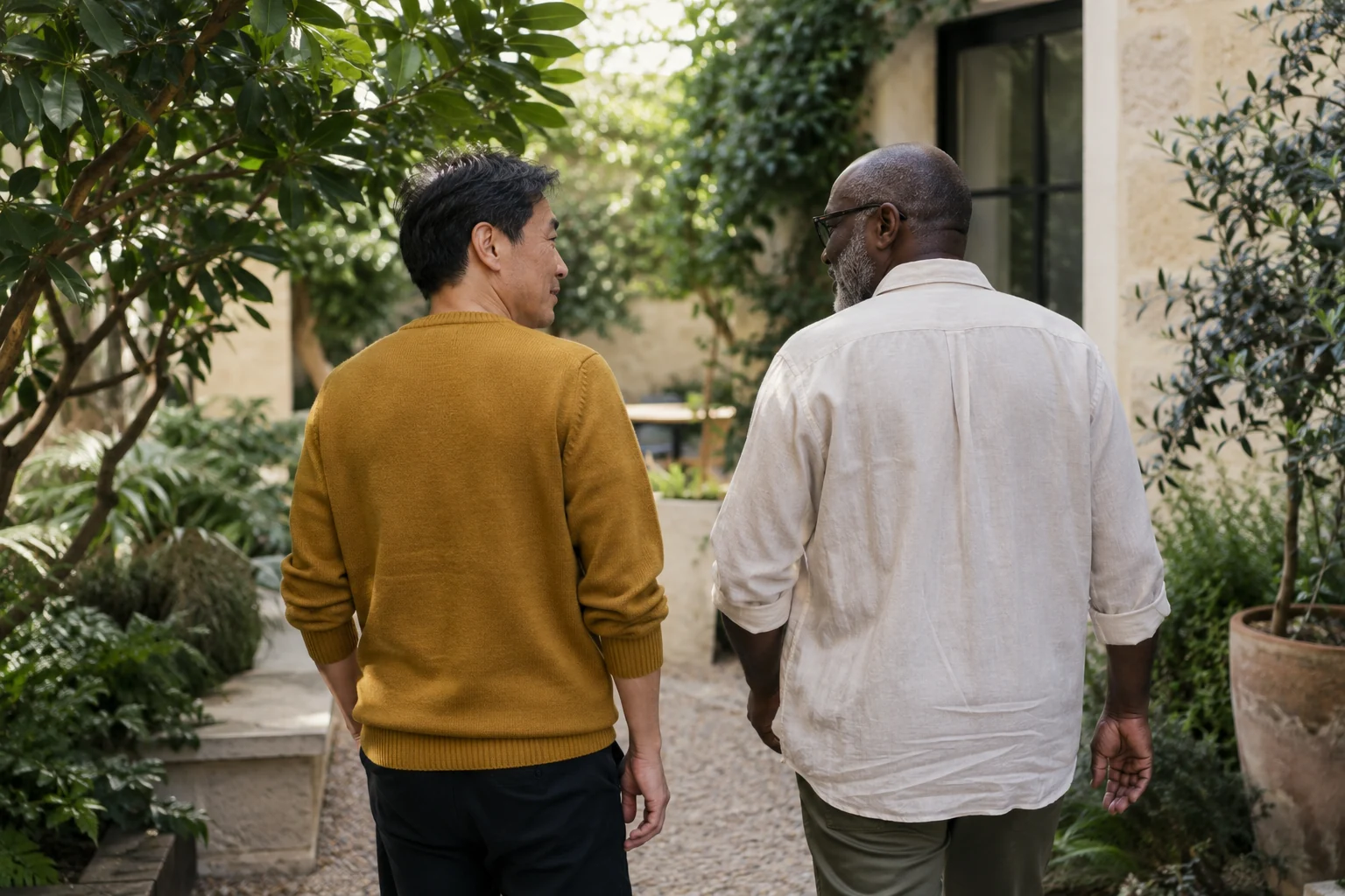 Two men walking and talking through a sunlit courtyard